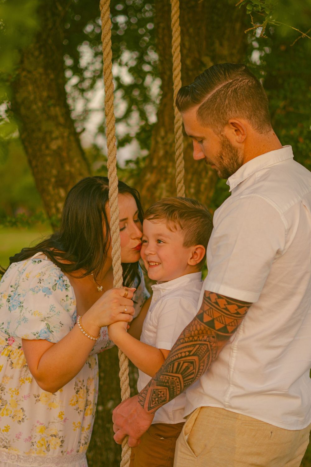 Family sharing playful moments on rope swing under tree during golden hour portrait session.