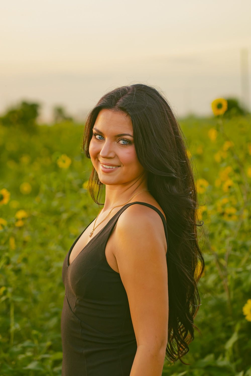 A graduate in black poses in a sunflower field during golden hour.