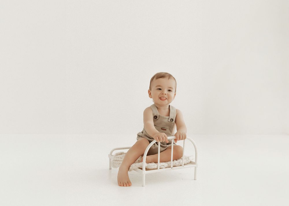 A small child sits and smiles on a white wooden sleigh against a neutral backdrop.
