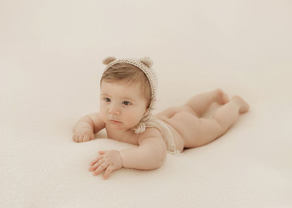 Adorable newborn baby lying on soft cream blanket during professional studio photography session.