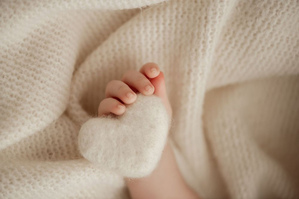 Tiny baby foot resting on soft white knitted blanket in gentle natural light.
