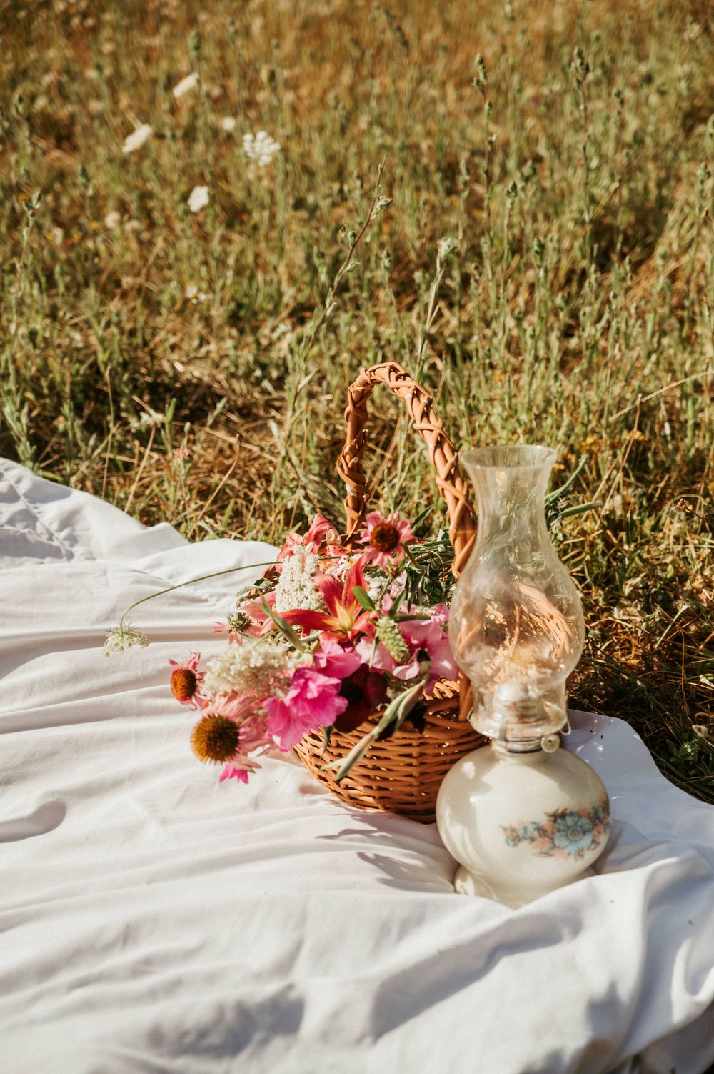 White picnic blanket with pink flowers and vintage decor on grass.