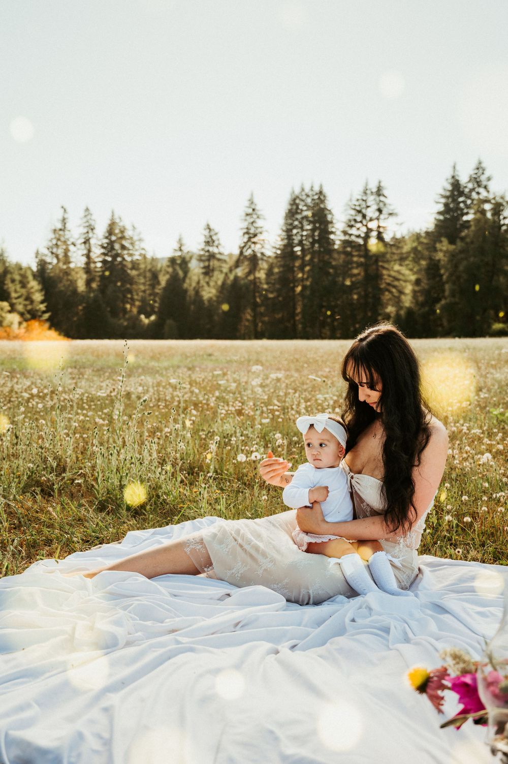 Sunset picnic scene in meadow with pine trees and white blanket.