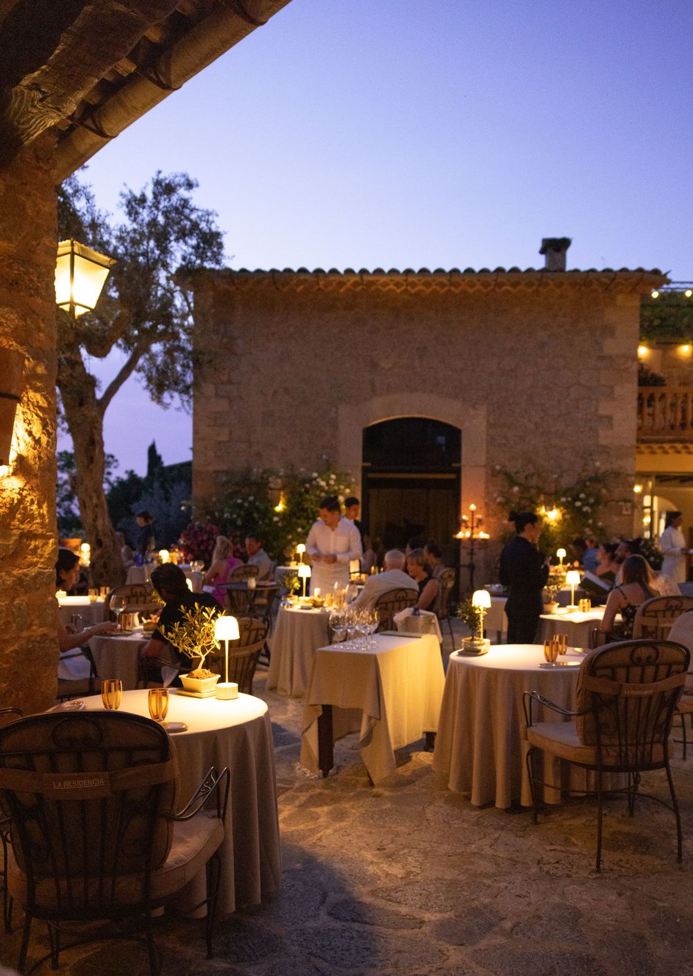 Mediterranean restaurant terrace with candlelit tables and stone walls at dusk creates romantic ambiance.