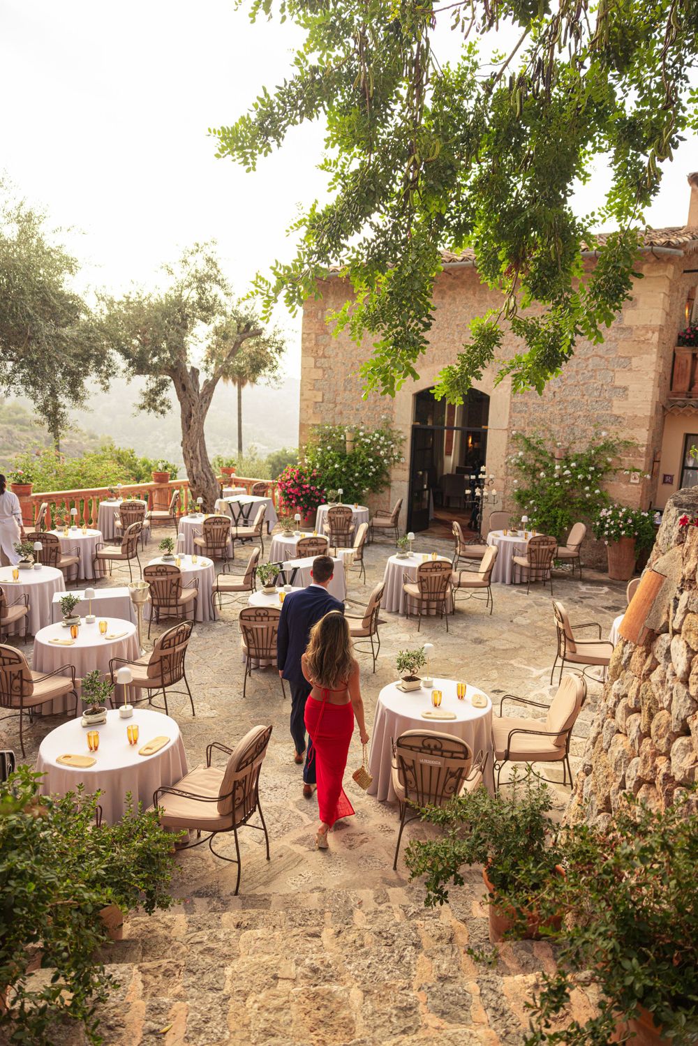 Rustic stone restaurant patio with round tables and wicker chairs set against mountain views.