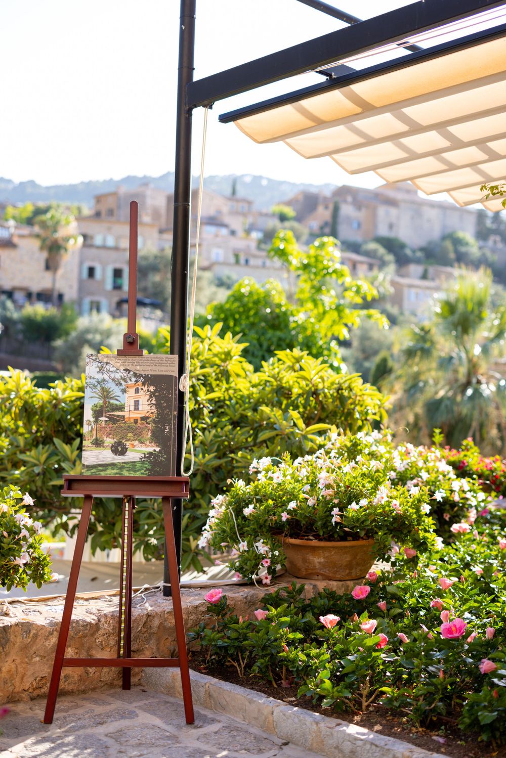 Artist easel on terrace with blooming garden and Mediterranean village views.