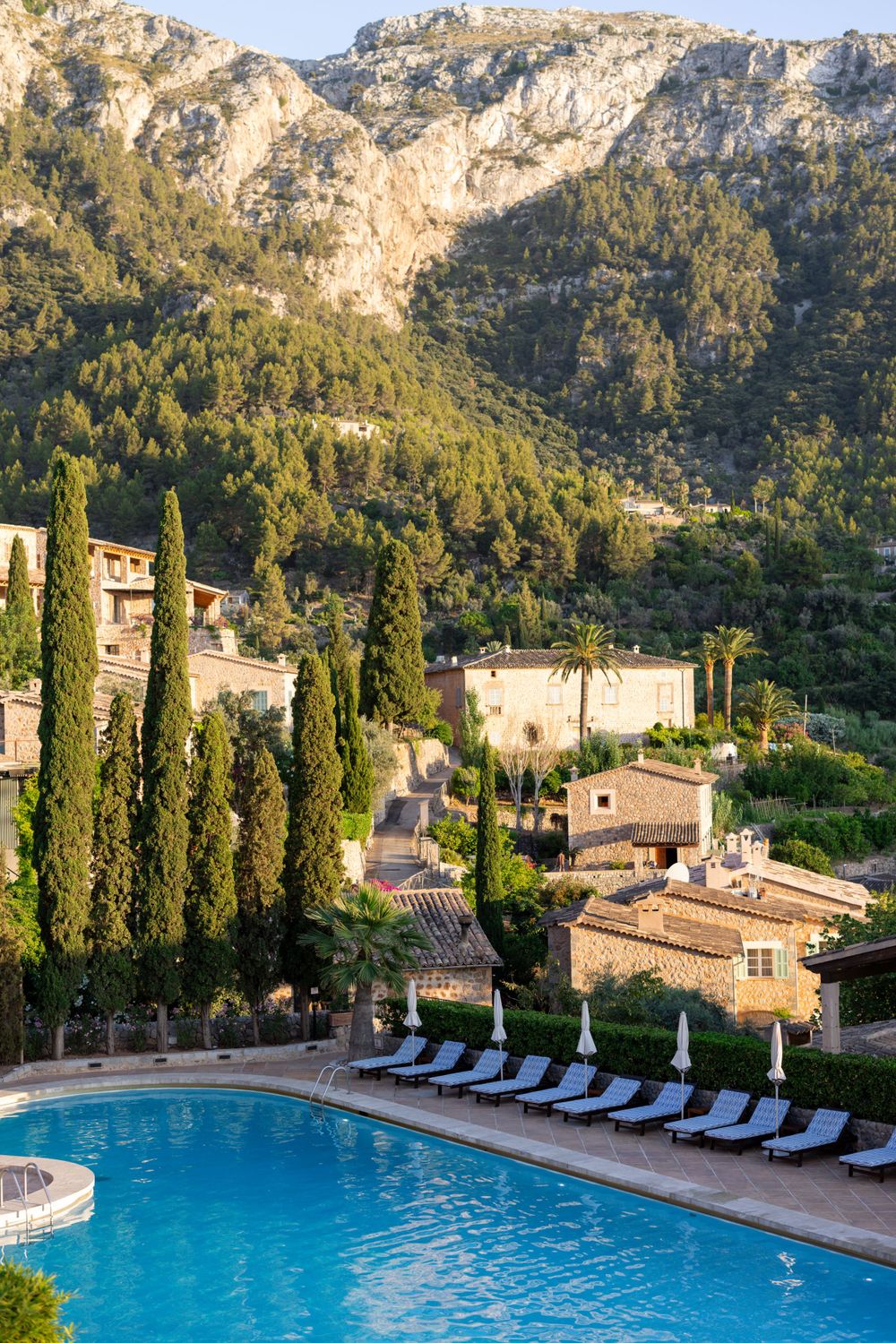 Resort swimming pool with loungers overlooking Spanish mountain village and cypress trees.