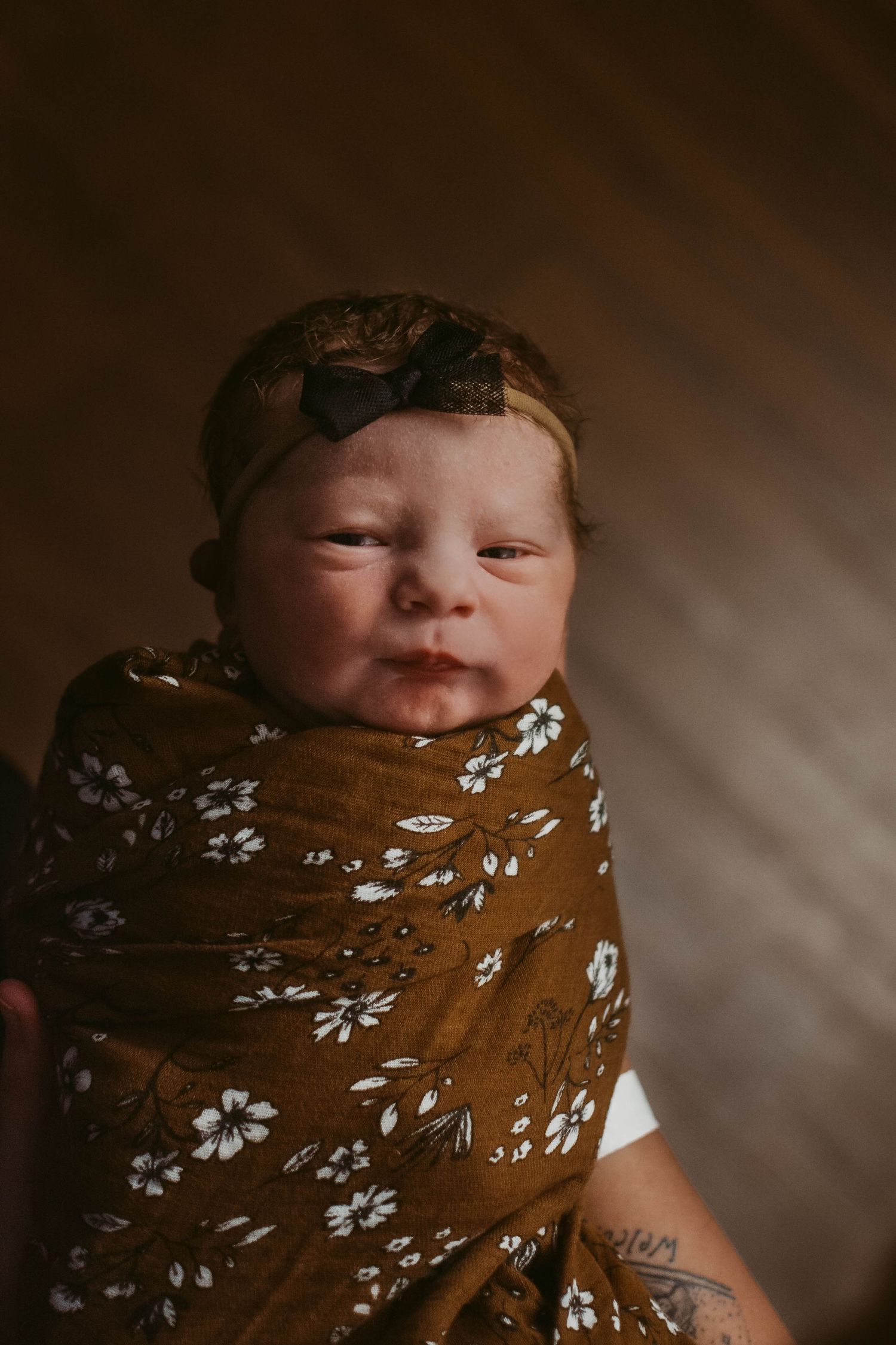 Newborn baby wrapped in brown floral swaddle wearing matching headband.