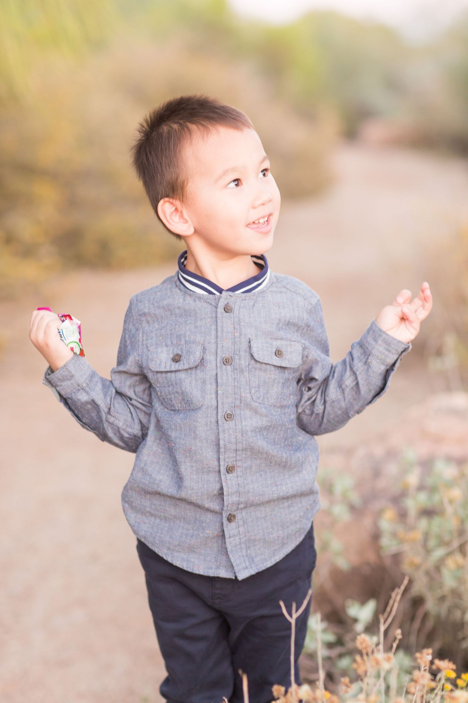 Young child in gray button-up shirt smiling and gesturing outdoors.