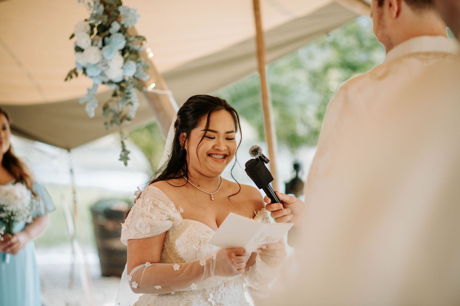 A joyful moment during wedding vows under an elegant tent with floral decorations.