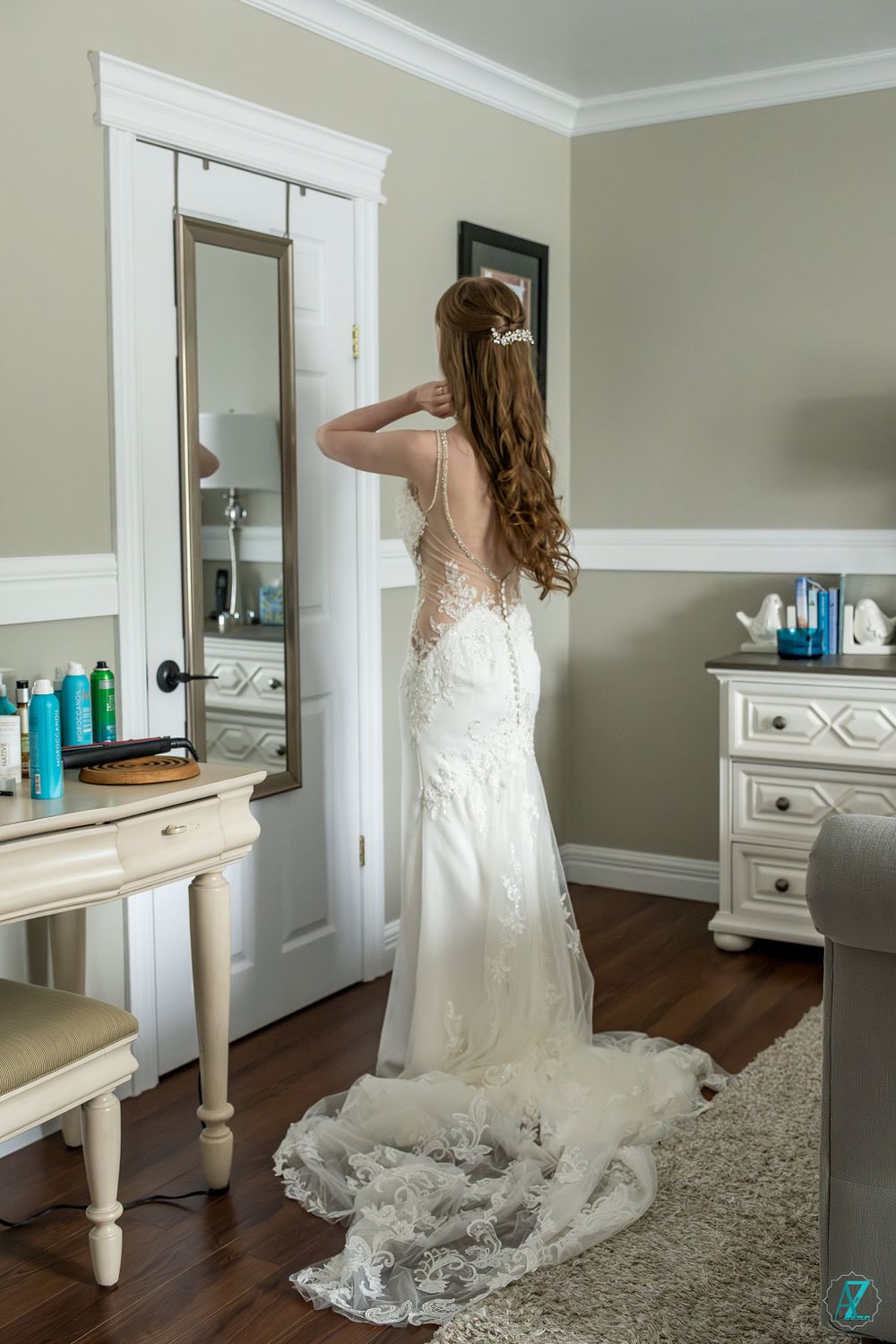 Elegant wedding dress with lace detail and train shown in a bedroom with vanity mirror.
