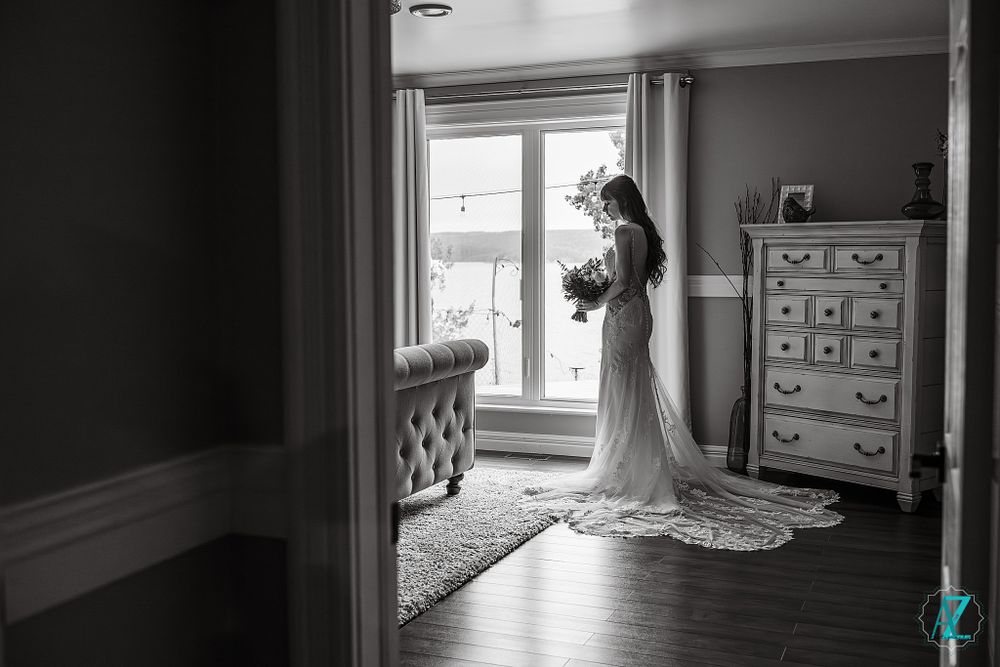 A silhouette of someone in a wedding dress stands by a window holding a bouquet.