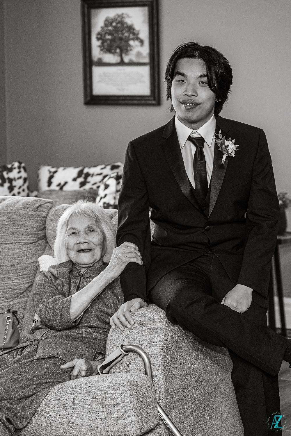 A touching black and white portrait of a young man in a suit with an elderly woman on a couch.