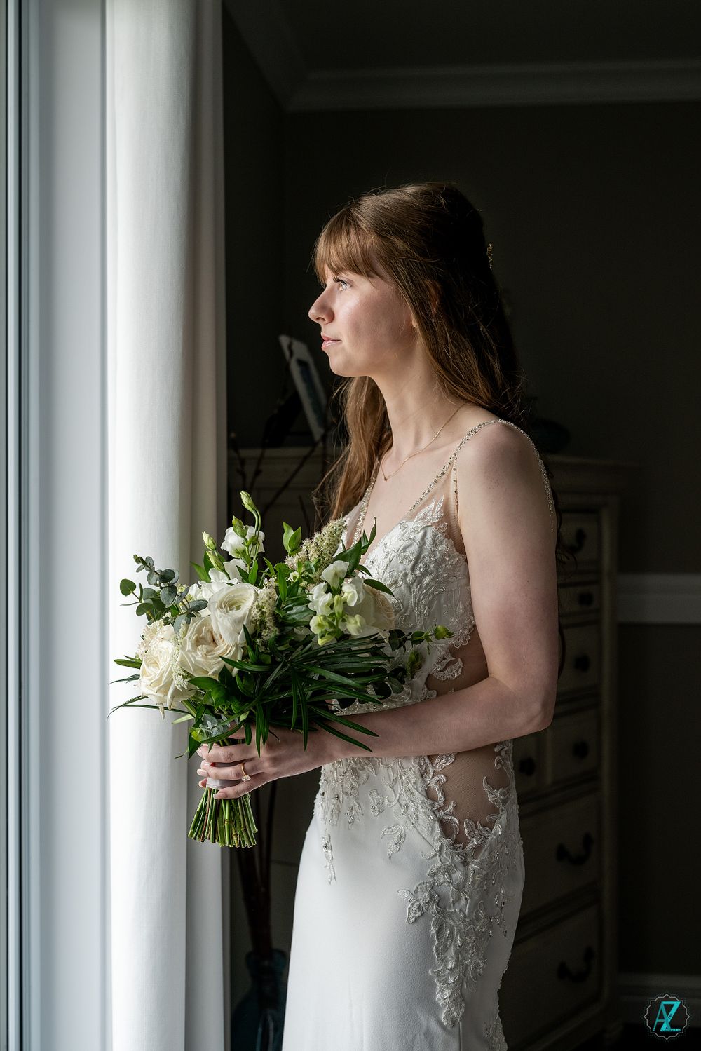 A serene bridal portrait by a window with natural light illuminating a beautiful white bouquet.