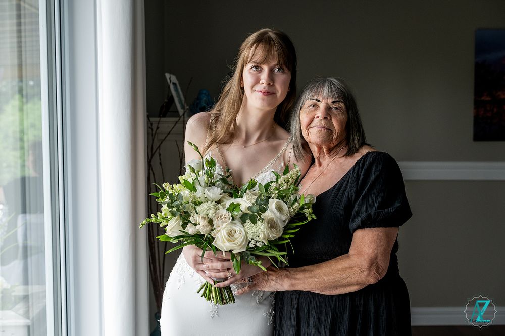 A wedding portrait showing two figures in formal attire holding a bouquet of white flowers by a window.