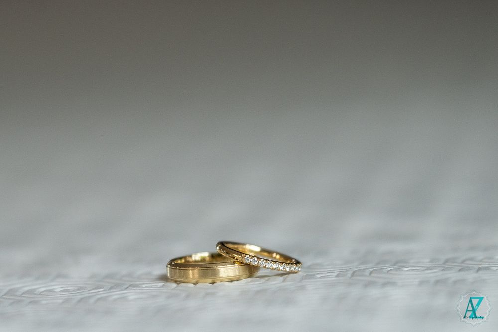 Two gold wedding rings photographed on a textured light gray surface.
