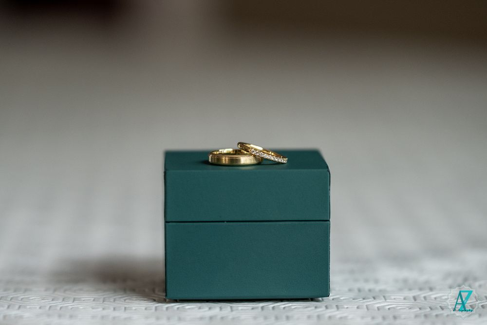 Gold wedding rings displayed on top of a teal green jewelry box.