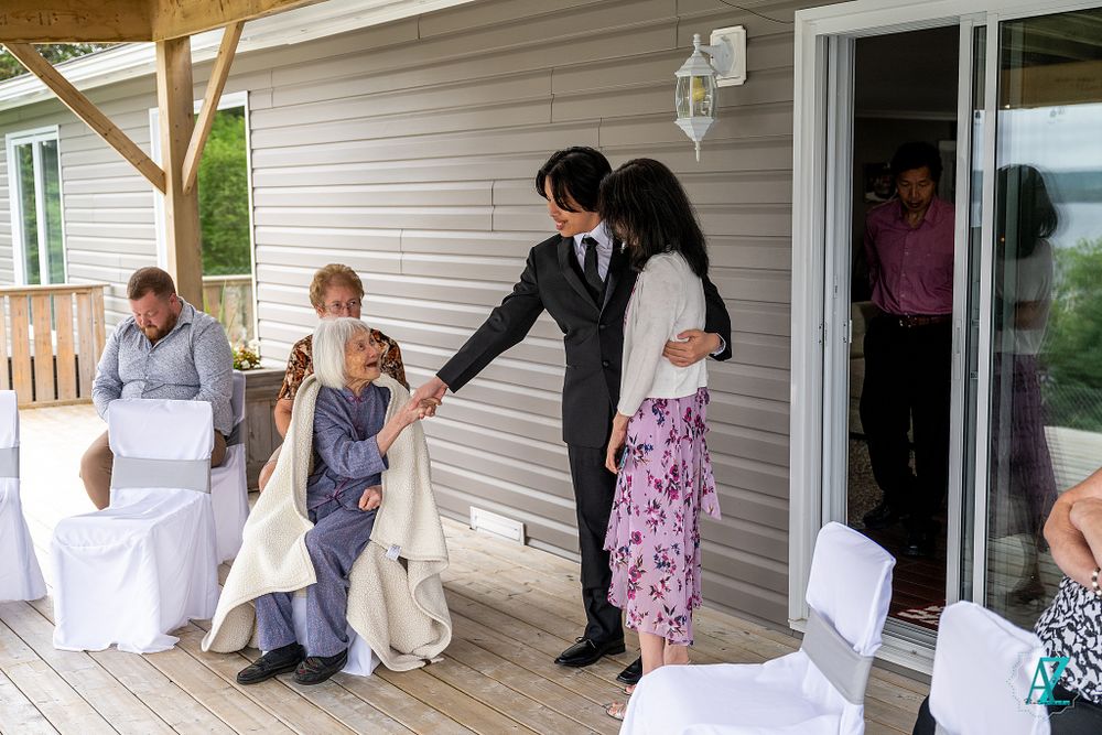 Wedding guests and participants socializing on a gray-sided porch during an outdoor ceremony.