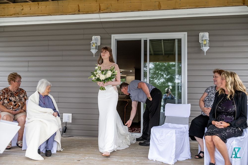 A wedding ceremony setup on a covered porch with white chairs and guests.