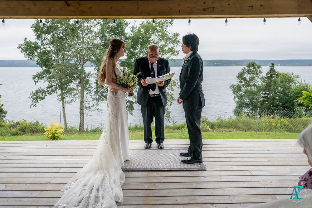 Intimate outdoor wedding ceremony on a covered wooden deck with waterfront views.