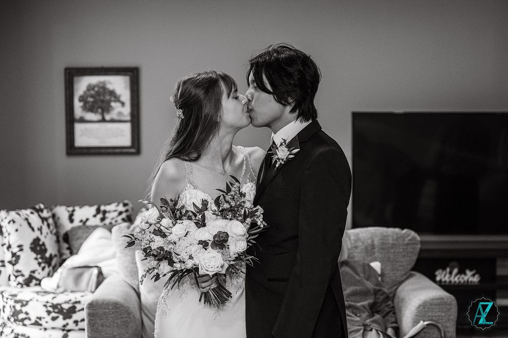 A romantic black and white wedding photo capturing a kiss while holding an elegant floral bouquet.