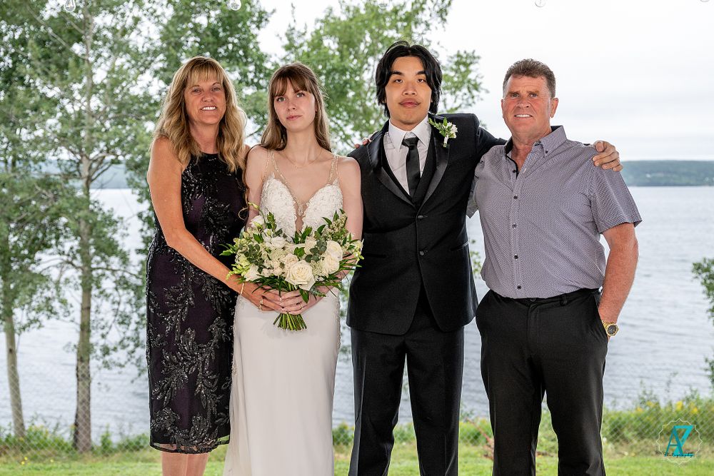 Wedding party poses together on lakeside deck with water and trees in background.