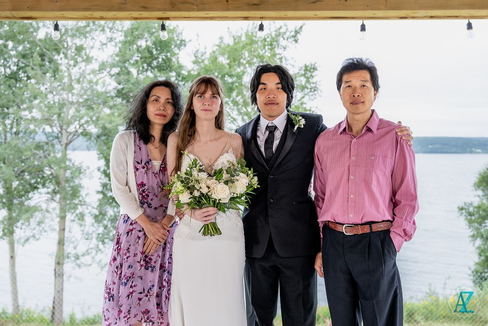 Wedding party poses outdoors against a lakeside backdrop with trees and natural scenery.