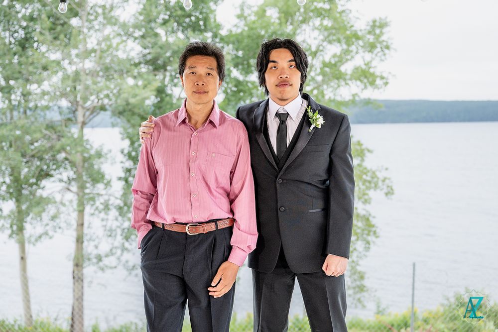 Two guests in contrasting formal attire pose outdoors with lake view behind them.