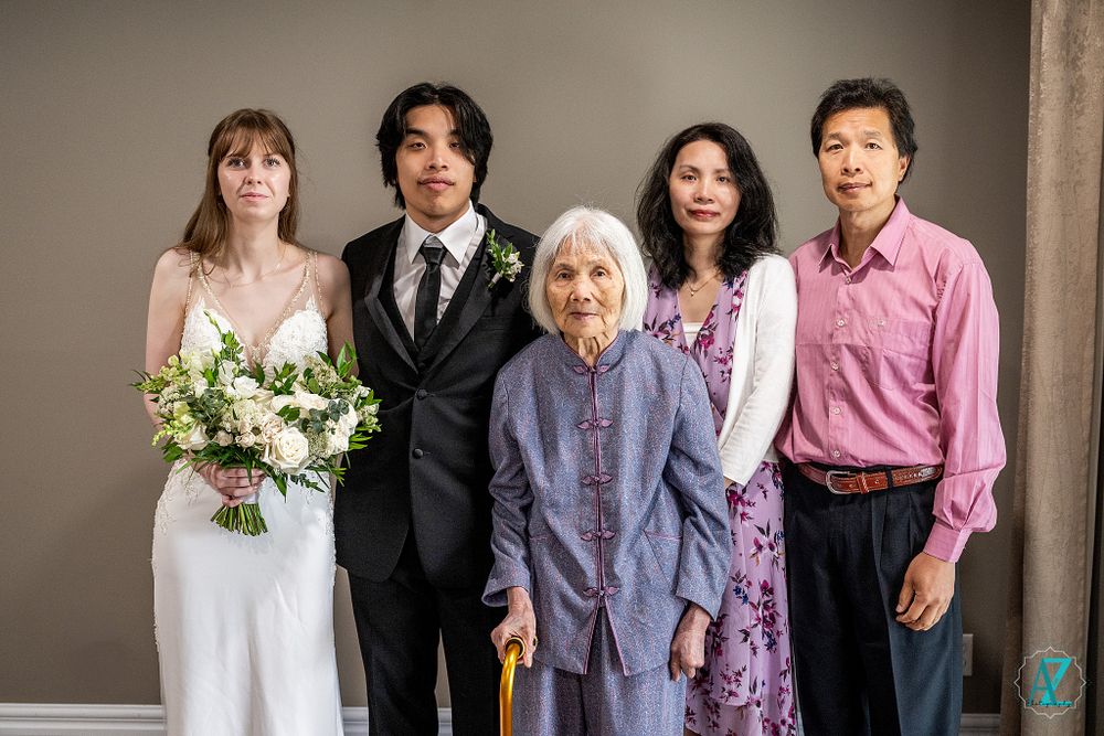 Wedding group photo in studio setting with cream colored backdrop and formal attire.