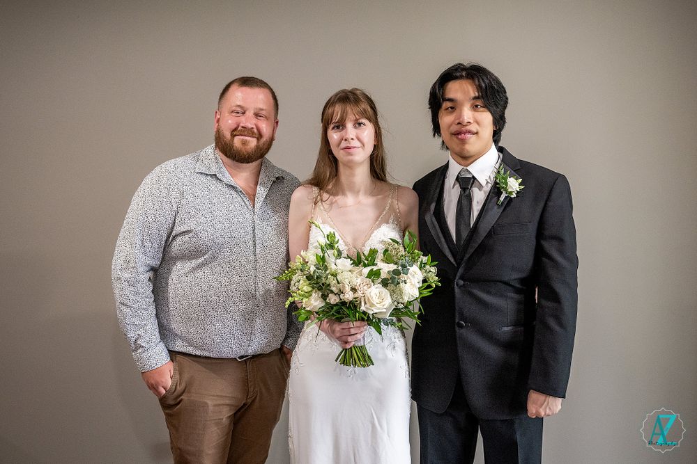 Three wedding guests pose together for formal portrait against neutral studio backdrop.
