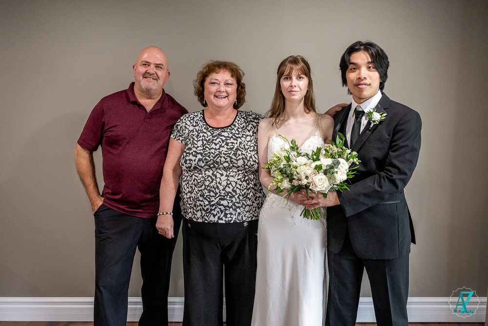 A formal group portrait at a wedding with two couples against a gray backdrop.