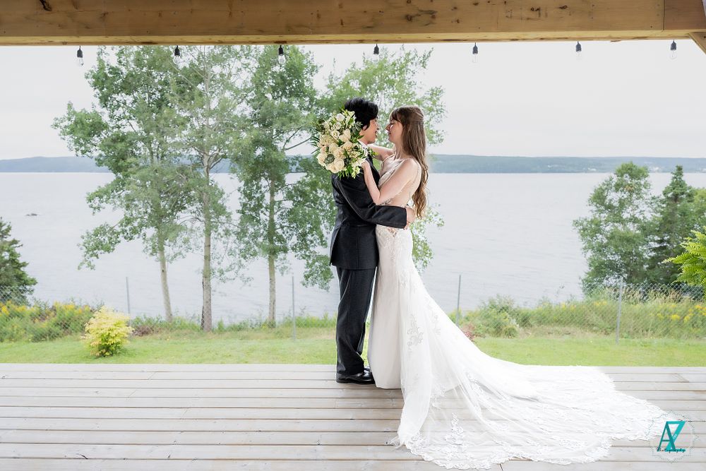 A romantic wedding photo of a couple embracing on a deck overlooking a lake.