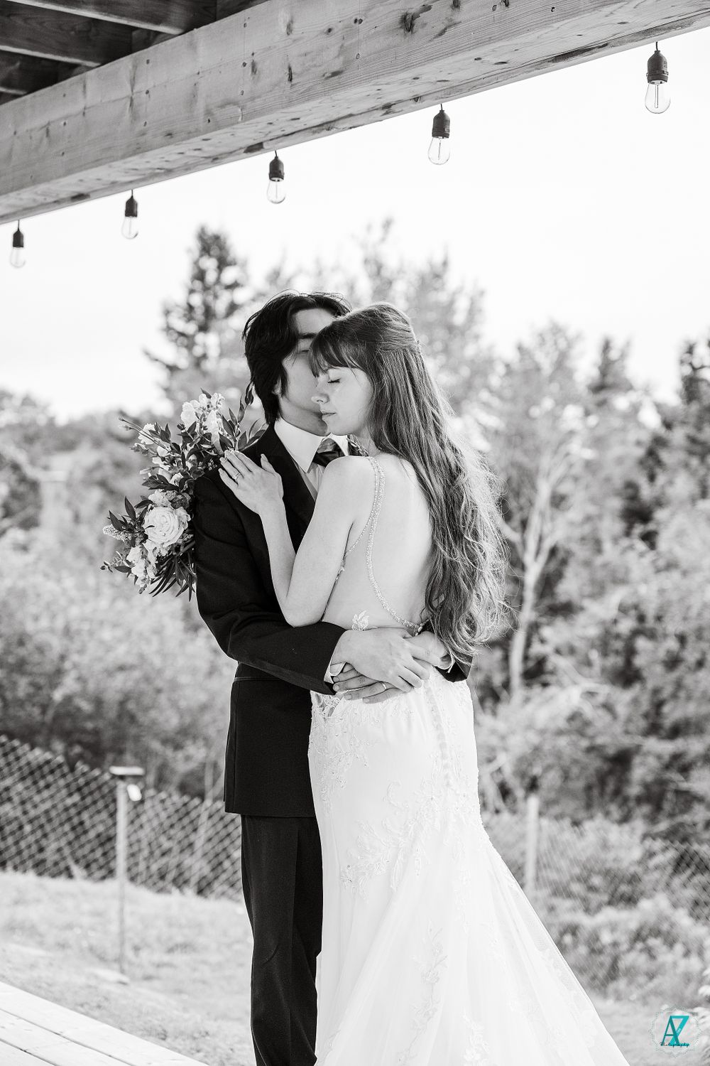 A black and white wedding portrait under wooden beams with string lights.