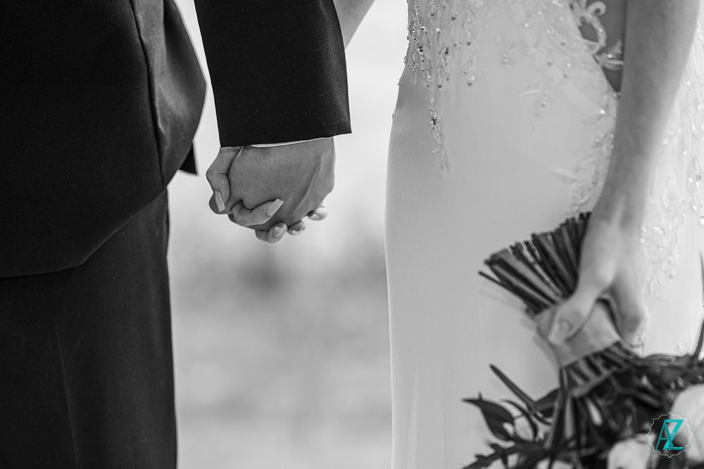 A close-up detail shot of newlyweds holding hands with a bouquet in frame.