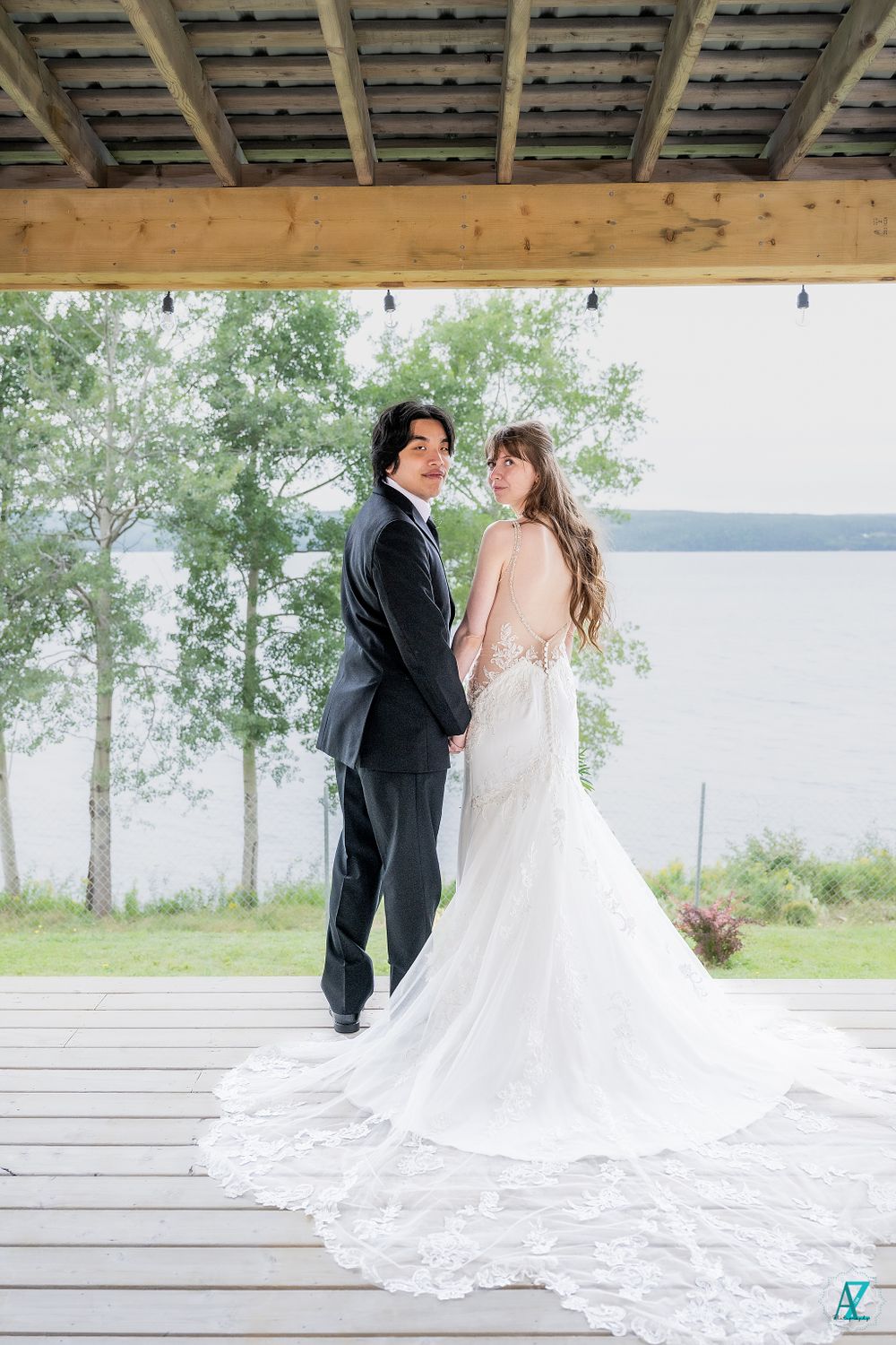 Wedding couple poses under wooden pergola with scenic lake view and flowing bridal gown.