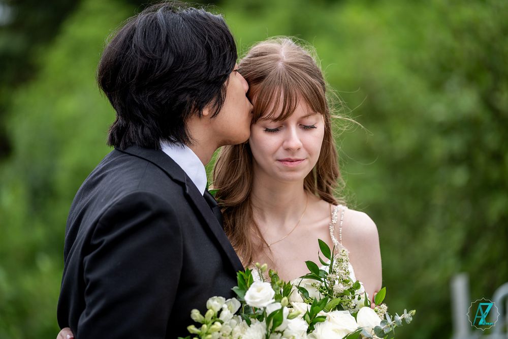 Intimate wedding moment captured outdoors with white floral bouquet and natural greenery.