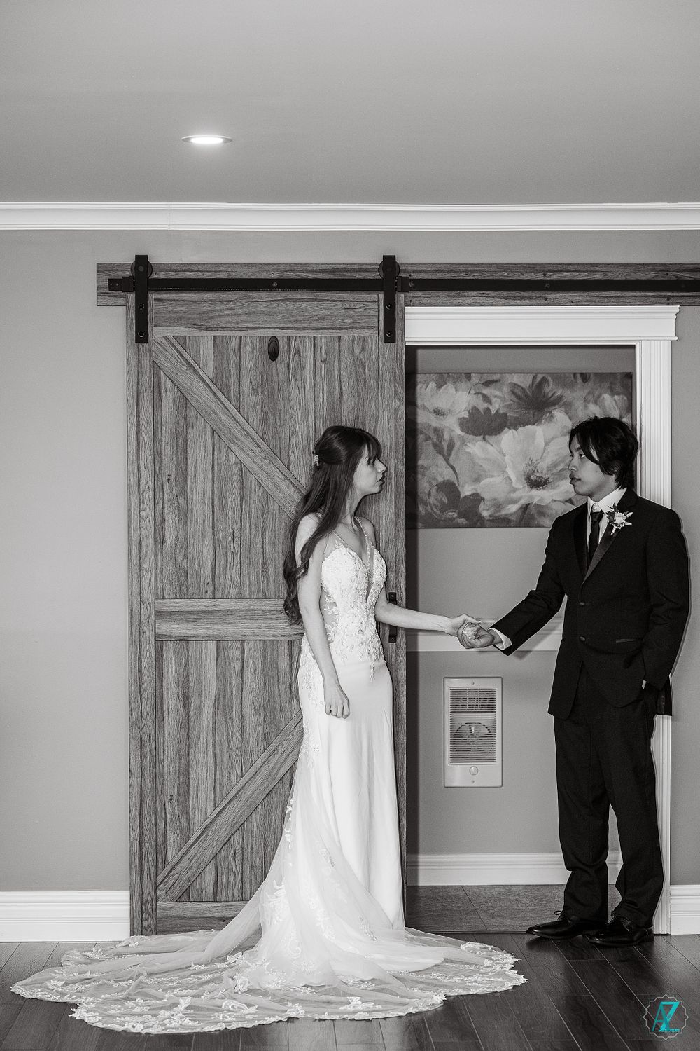 Black and white wedding photo of couple by rustic sliding barn door in formal attire.