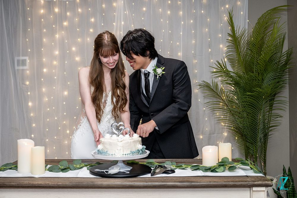 Couple smiling while cutting their wedding cake at a decorated reception table.