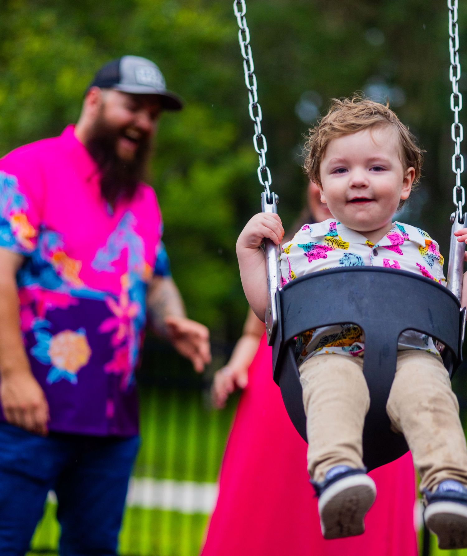 A child enjoys swinging at a playground while an adult in bright clothing stands nearby. Oviedo, Florida