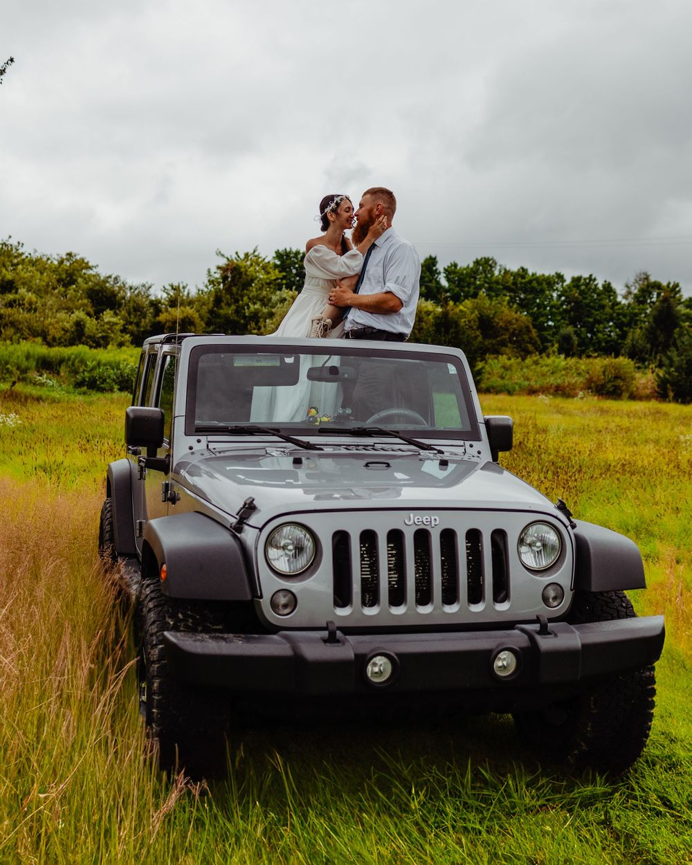 Silver Jeep Wrangler parked in tall grass field during cloudy wedding photoshoot.