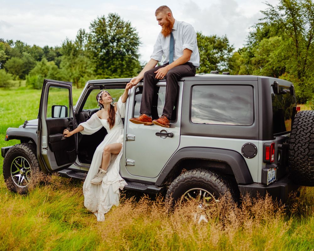 Casual wedding photos with silver Jeep Wrangler in green field setting.