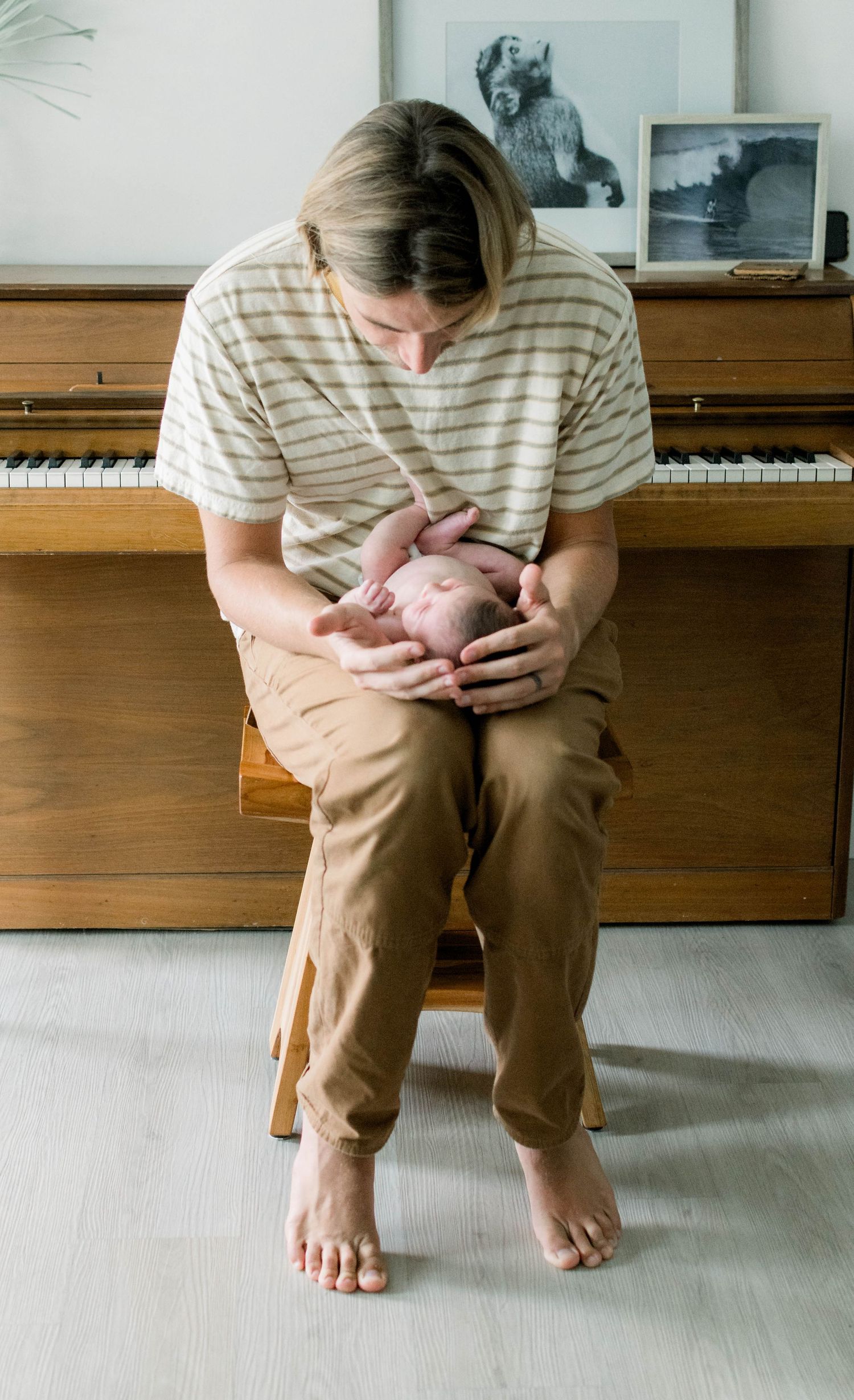 A person in a striped shirt sits at a piano bench holding something close.