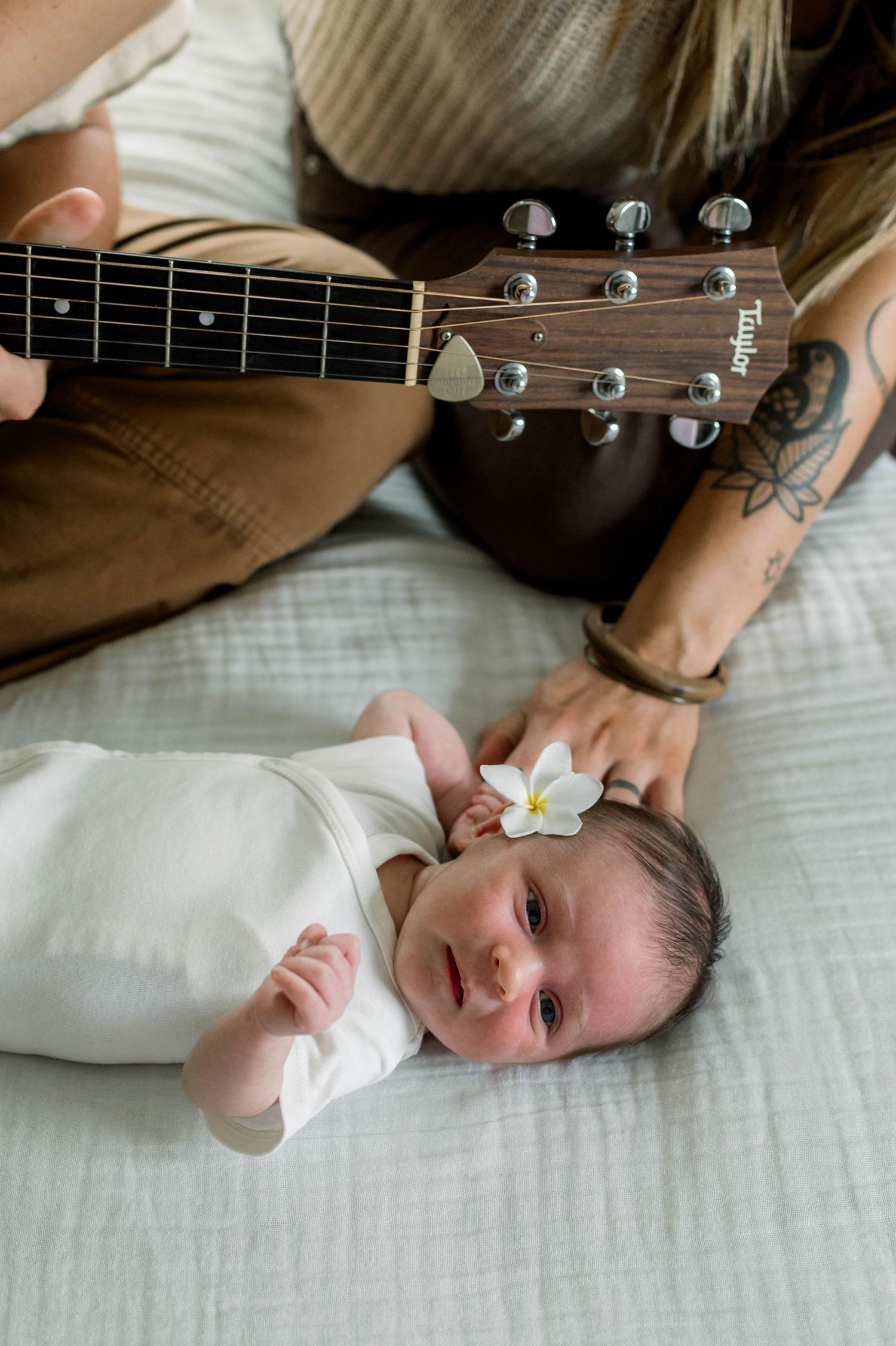 Acoustic guitar neck shown next to sleeping newborn with small white flower.
