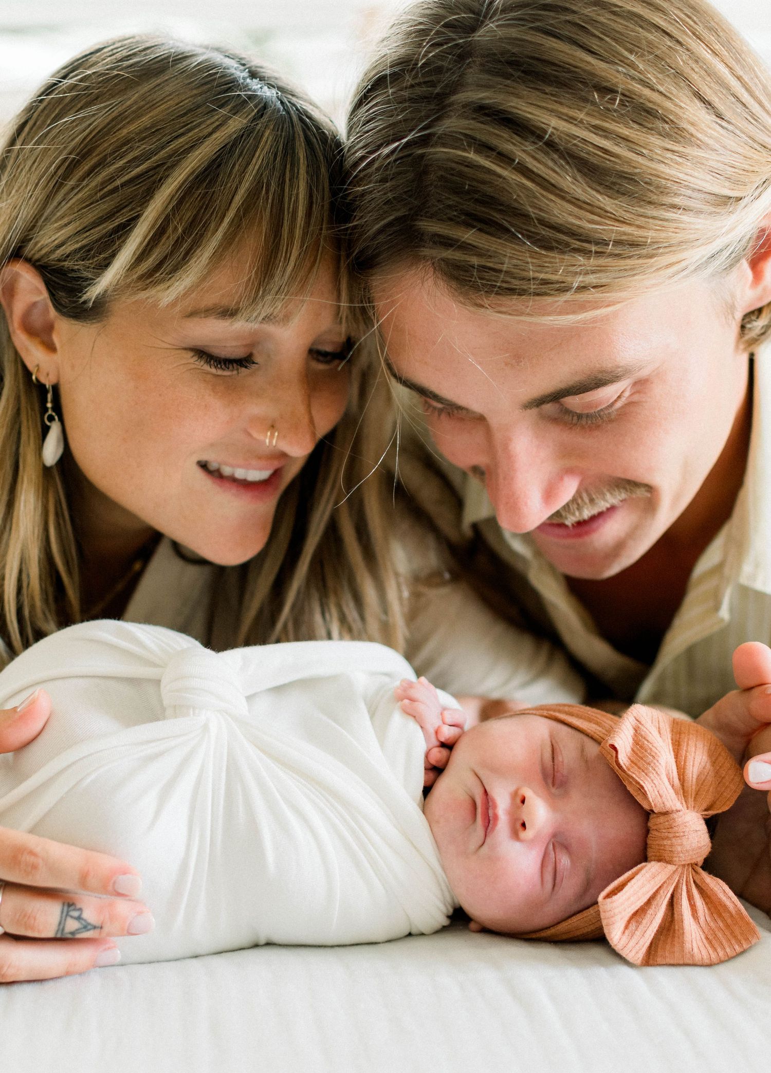 Intimate lifestyle newborn photography with soft white bedding and peach accents.