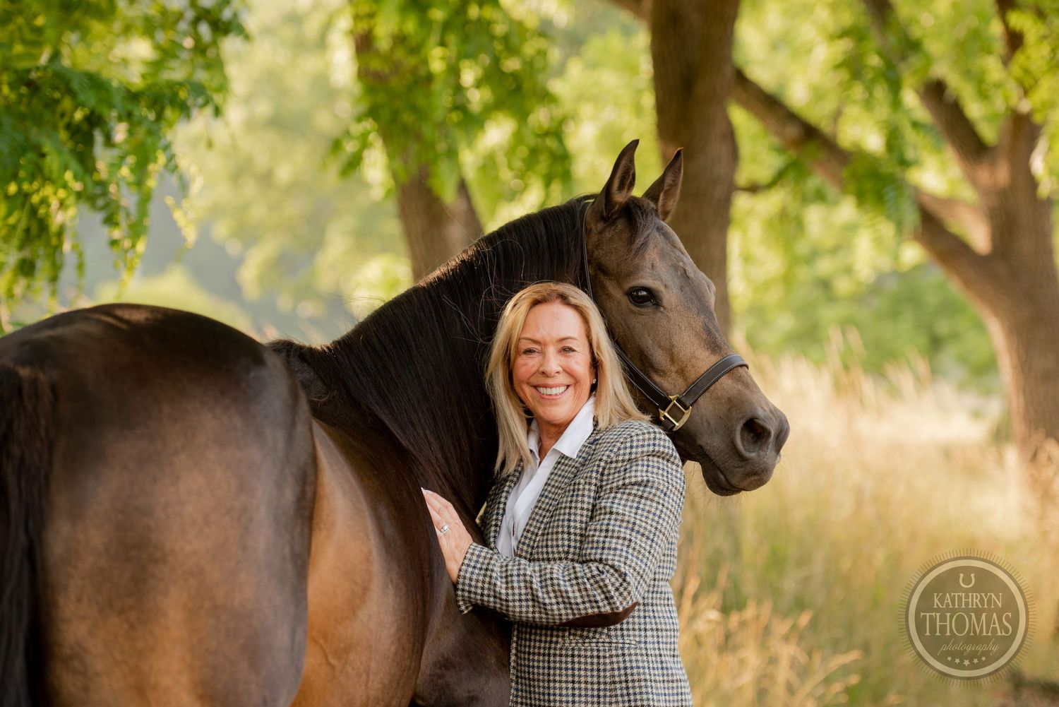 Handler in tweed jacket stands with elegant dark horse against natural backdrop.