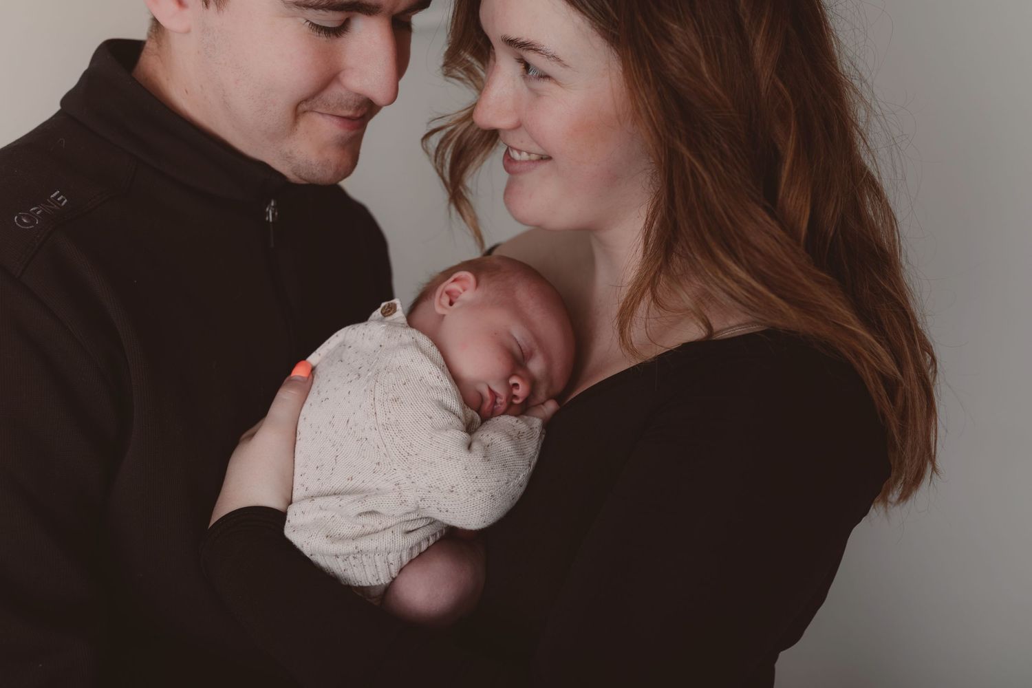 Intimate family portrait with sleeping newborn against grey background.