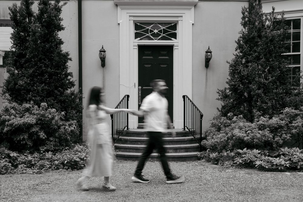 Black and white photo of a couple walking past an elegant building entrance with steps and lanterns.