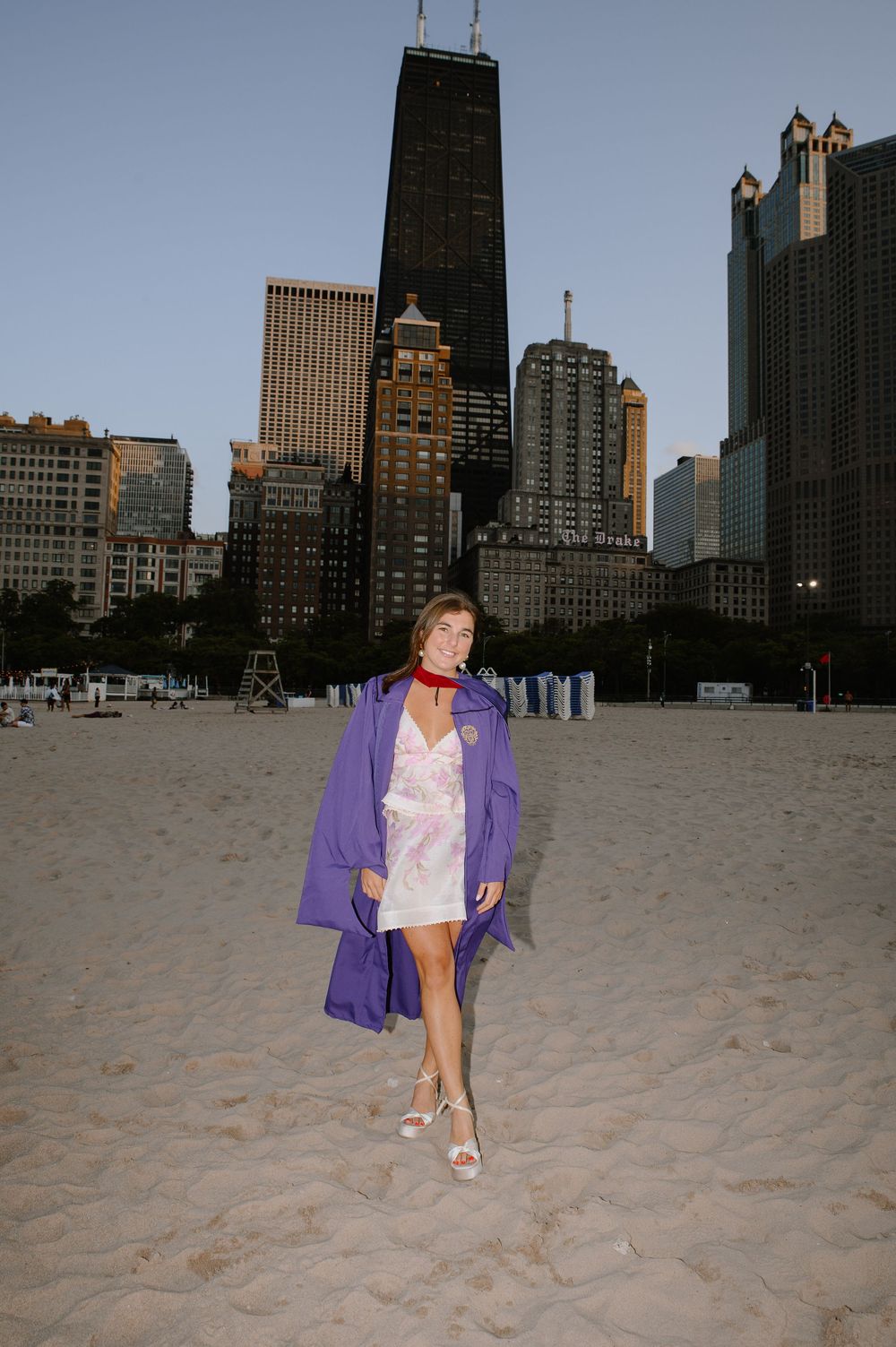 A person in a purple jacket poses on a beach with Chicago's iconic skyline in the background.