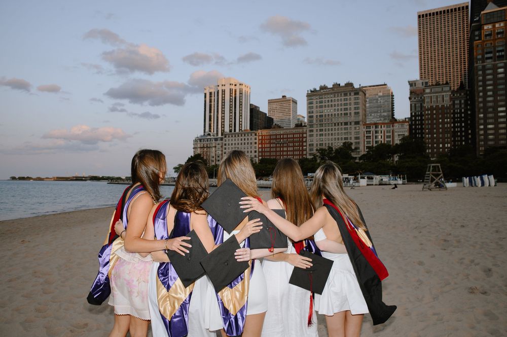 A group of friends huddle together on a beach with city skyscrapers visible in the background at sunset.