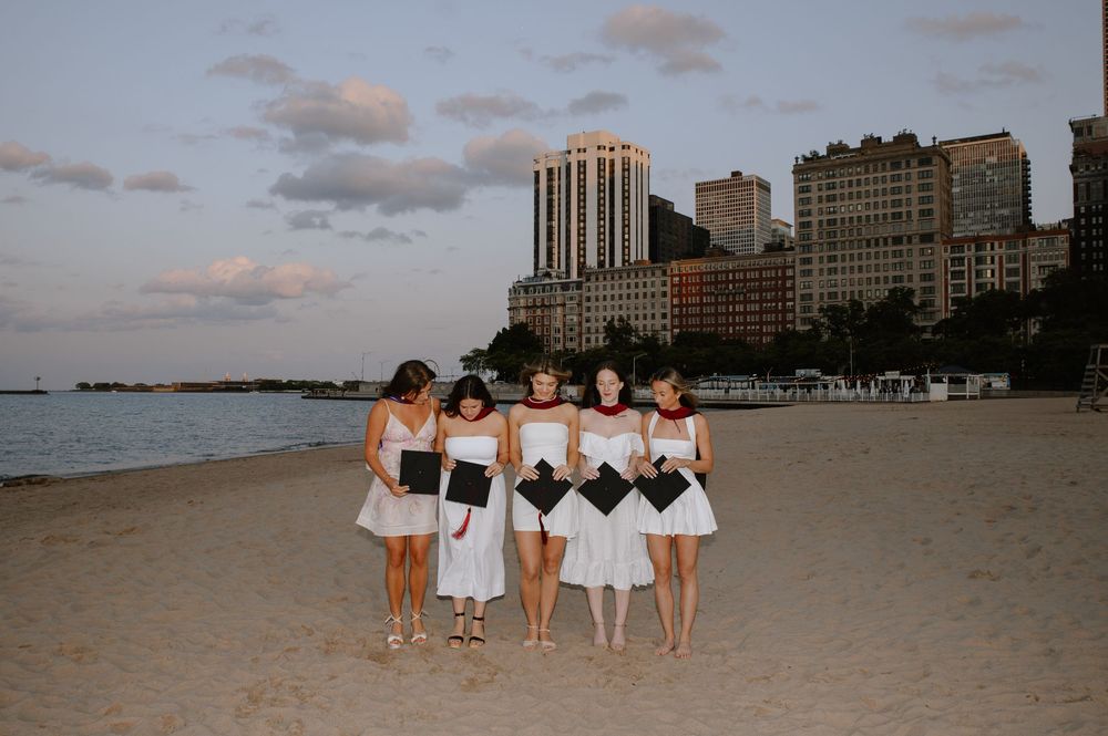 A group in matching white outfits stands together on a beach at sunset with city buildings in the background.